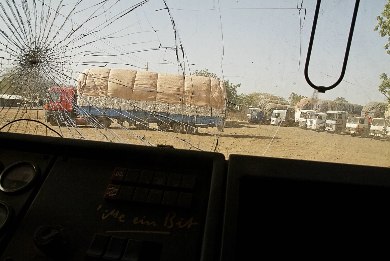 Camiones aparcados delante de la planta de procesamiento de algodón, vistos desde el parabrisas agrietado de otro vehículo (K. Gómez)