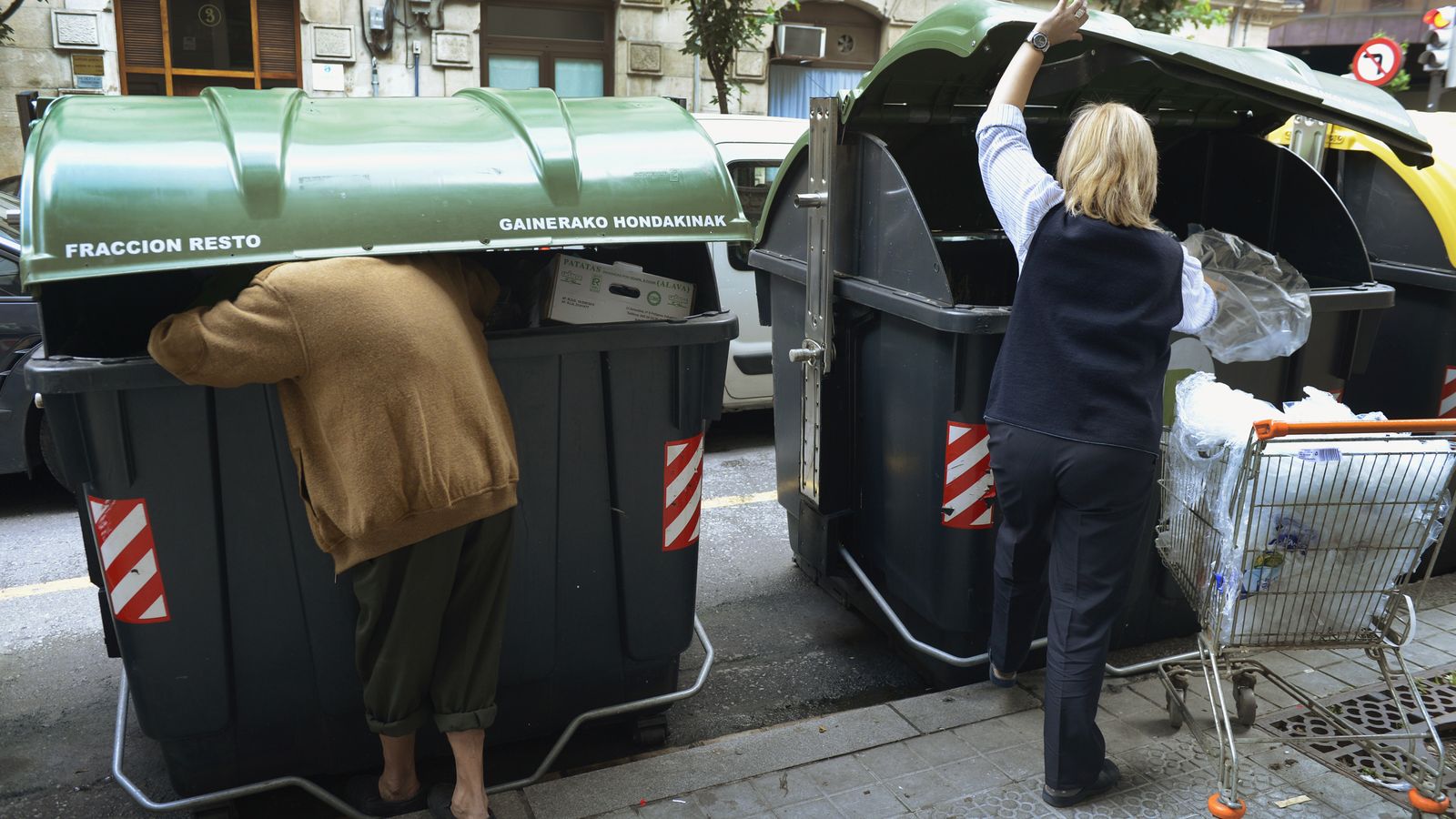 Foto: Un hombre busca comida en un contenedor de Bilbao mientras un empleado de un supermercado tira comida en el de al lado. (Reuters)