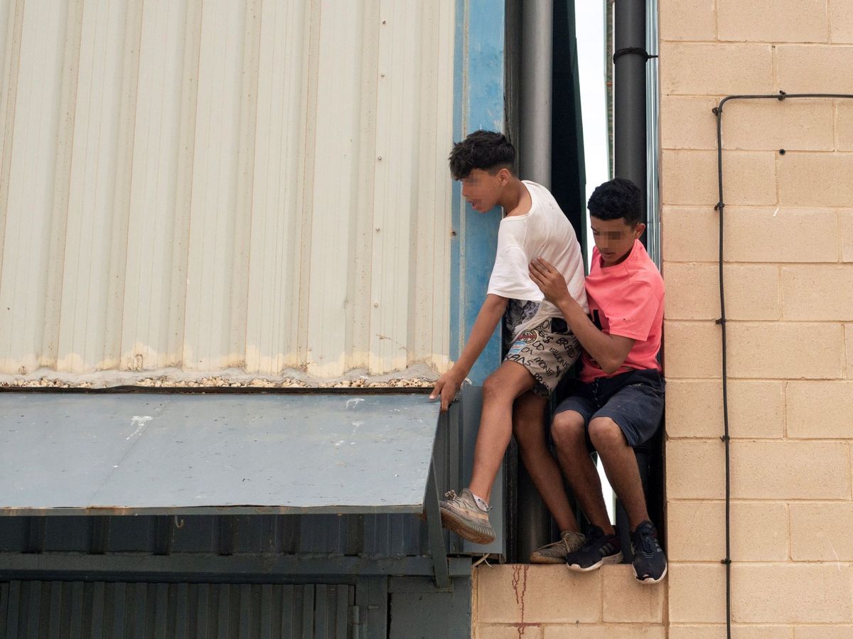 Foto: Dos migrantes se escapan de la nave del polígono industrial cercano a la playa de El Tarajal. (EFE)