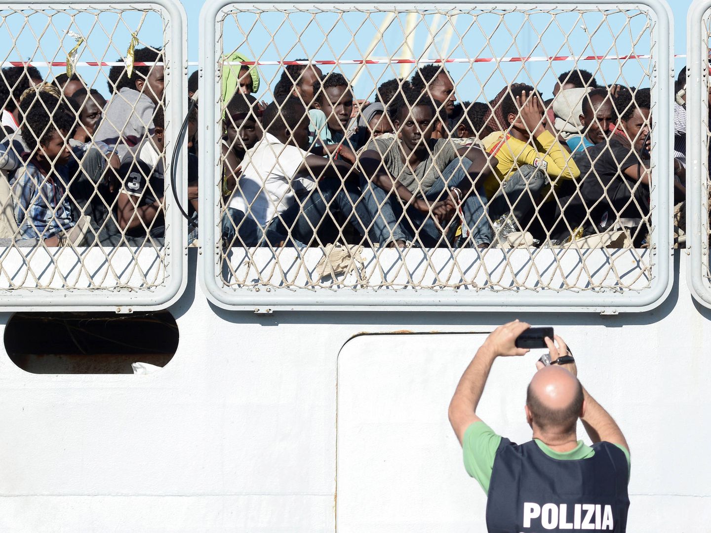 Un agente de policía fotografía a un grupo de inmigrantes que esperan para desembarcar en el puerto de Palermo. (Reuters)