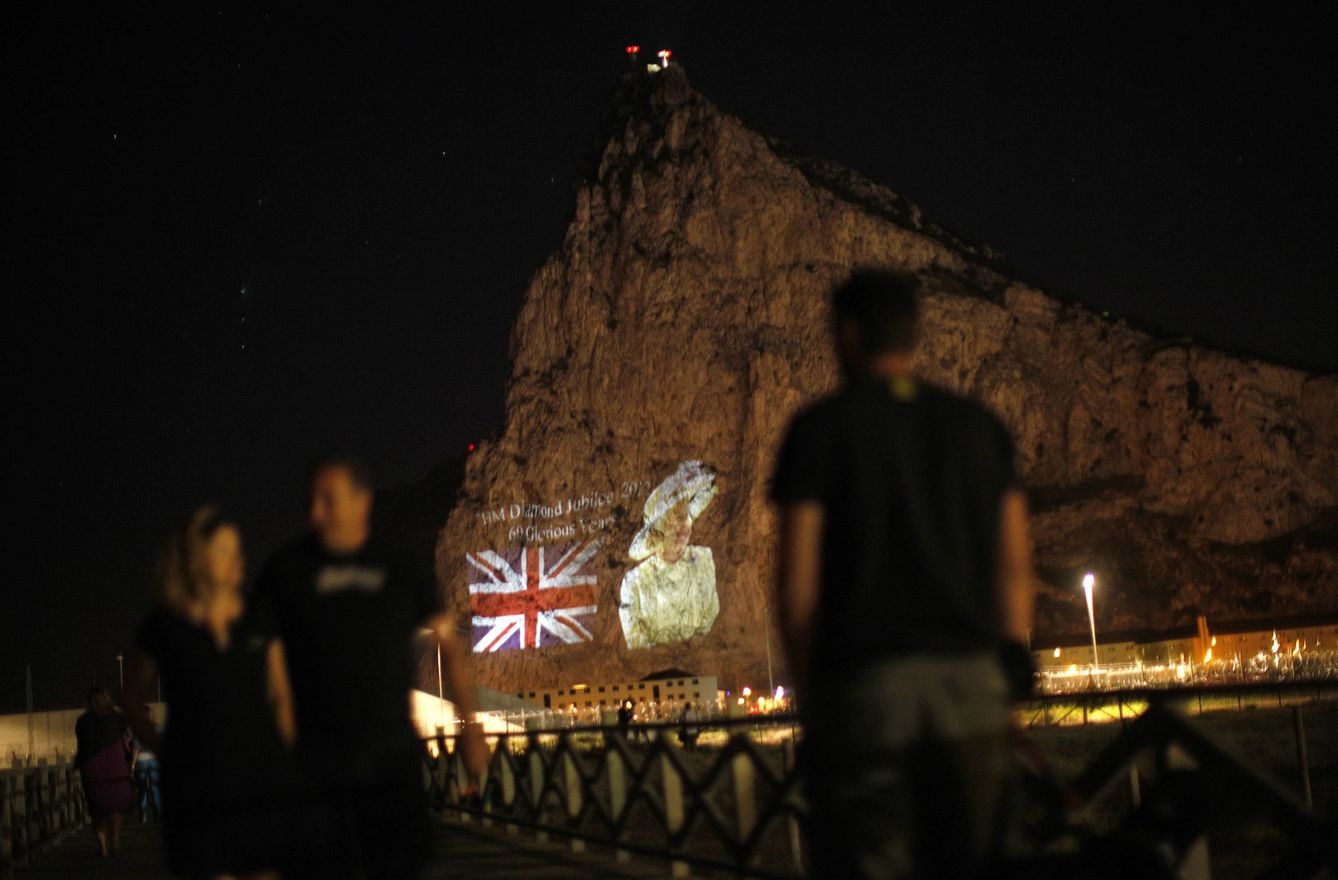 Varias personas observan una imagen de Isabel II y la bandera británica en el Peñón. (Reuters)