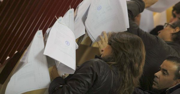 Foto: Varios ciudadanos consultan en las listas de un colegio electoral de Madrid la mesa en la que deben votar. (EFE)