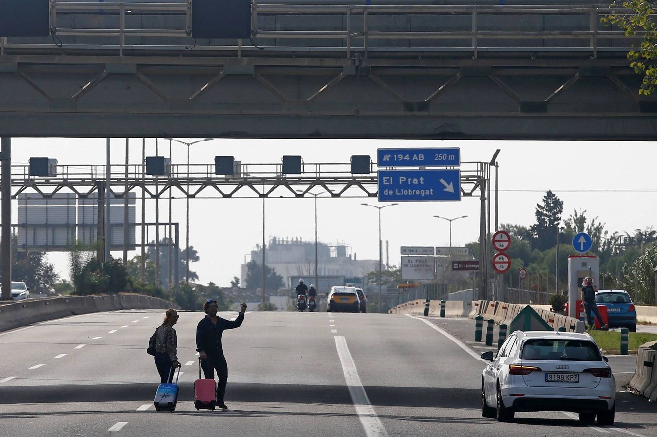 Dos viajeros tratan de llegar al aeropuerto de El Prat, bloqueado por los manifestantes. (EFE)