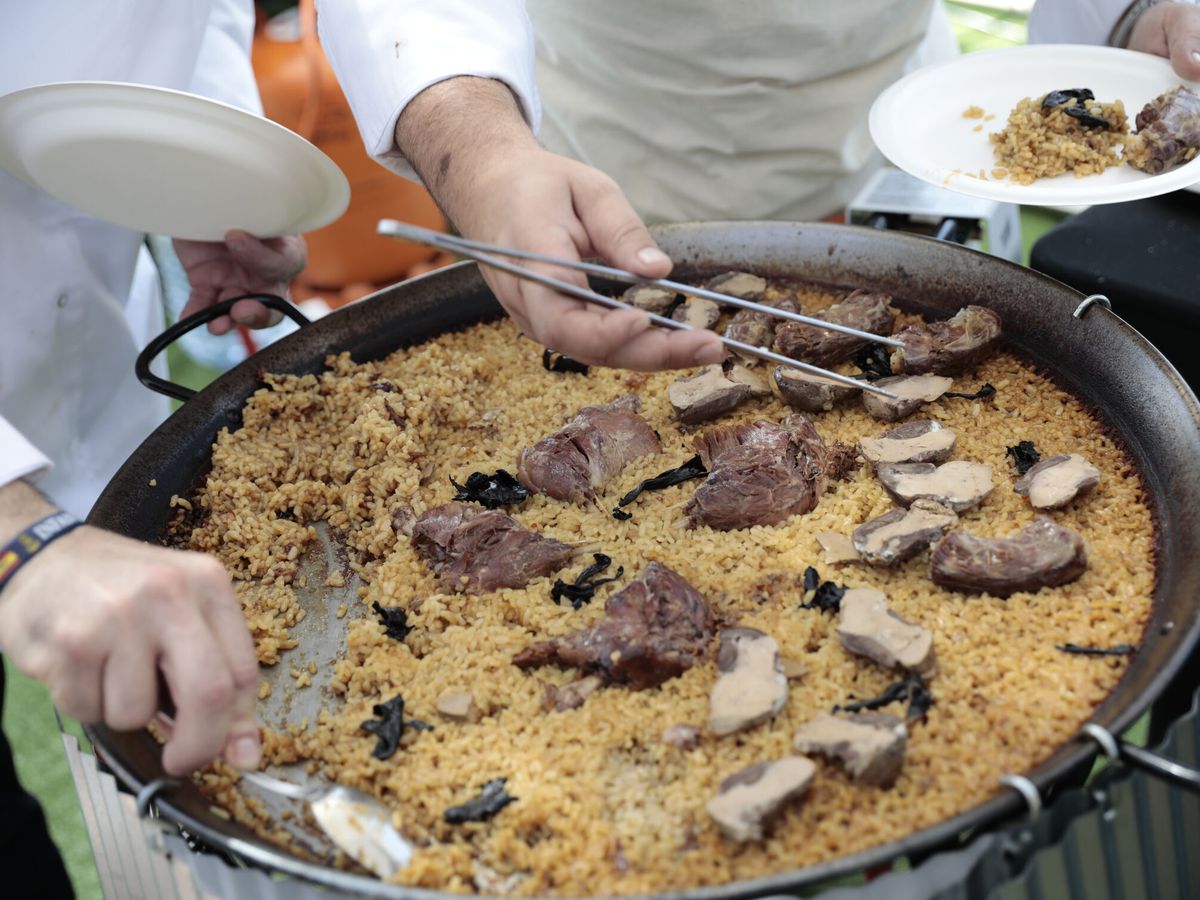 Foto: Dos cocineros sirven una paella en el World Paella Day. (EFE/Ana Escobar)