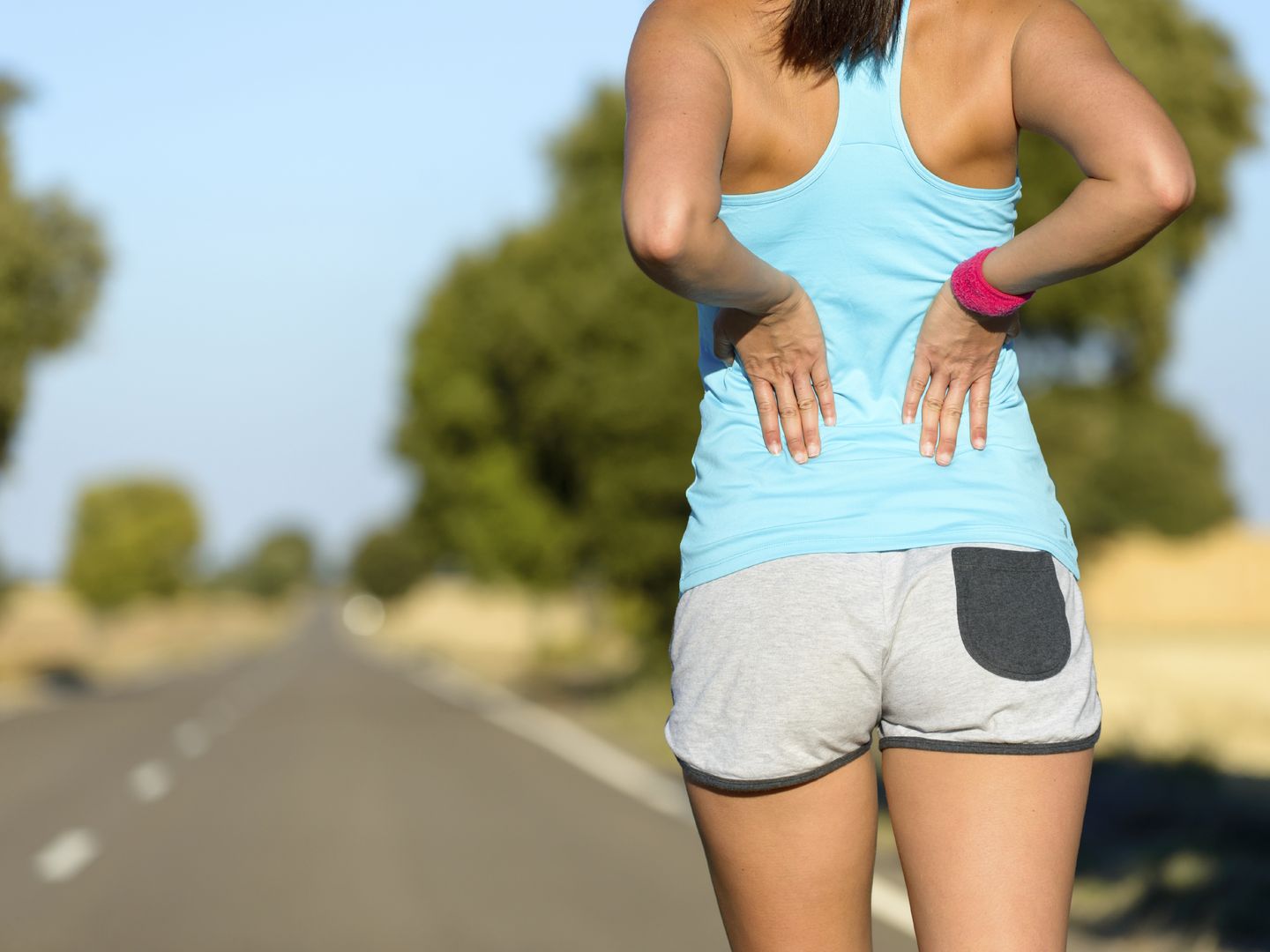 Female runner athlete low back injury and pain. Woman suffering from painful lumbago while running in rural road.