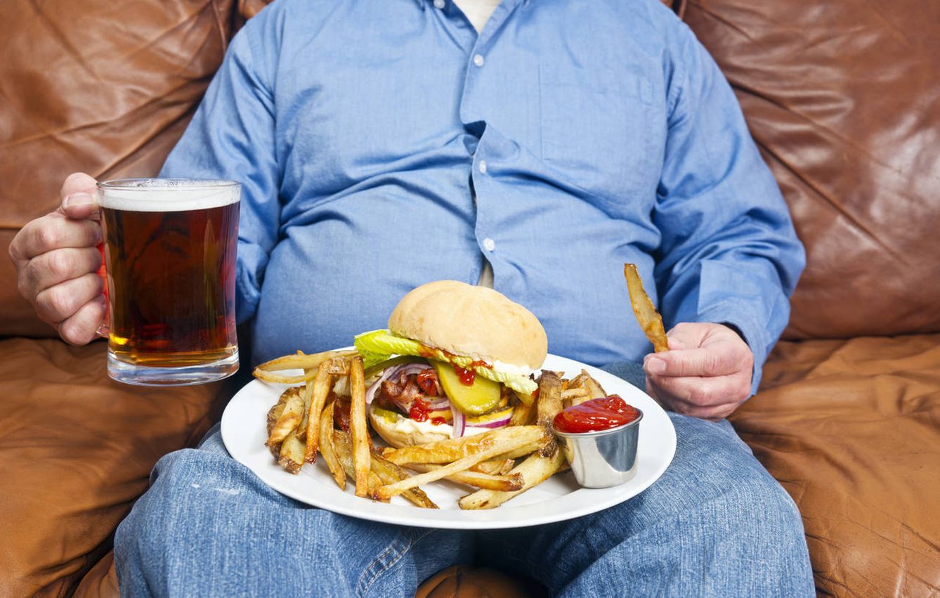 Un señor se come una hamburguesa en su sofá. (iStock)