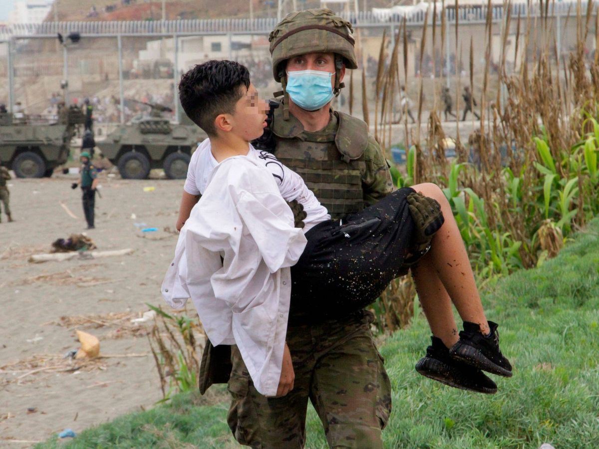 Foto: Un soldado del Ejército de Tierra ayuda a un menor en Ceuta. (EFE)