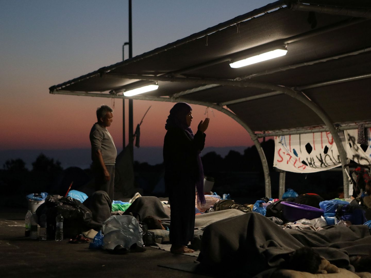 Inmigrantes rezando al amanecer mientras esperan a ser trasladados a otro campamento. (Reuters)