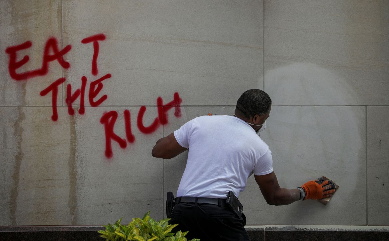 Una persona limpia un grafiti donde pone 'Comerse a los ricos'. (Reuters)
