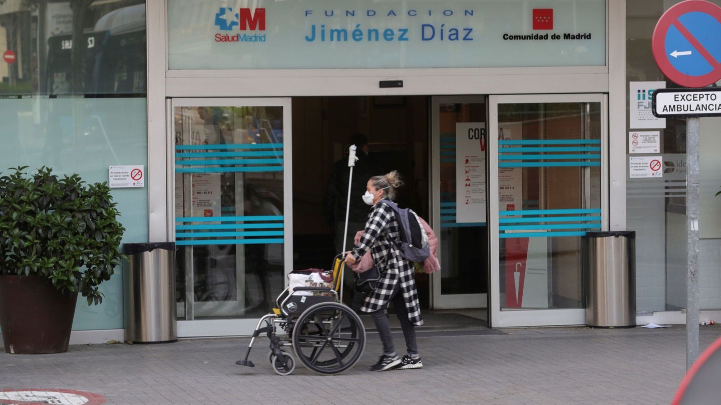 Una mujer con una máscara sanitaria porta una silla de ruedas en los exteriores del Hospital Universitario Fundación Jiménez Díaz de Madrid. (EFE)