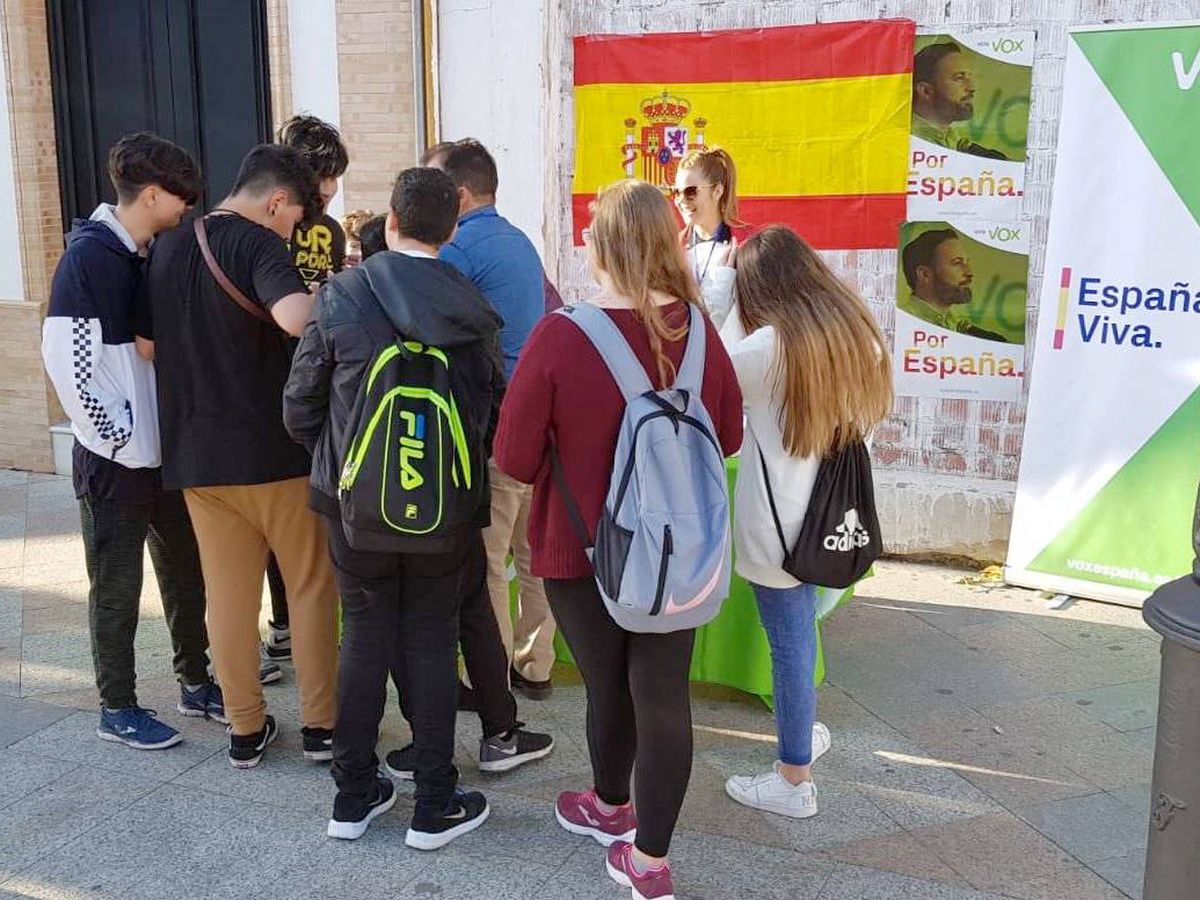 Foto: Grupo de jóvenes en Los Palacios frente a un cartel de Vox. 