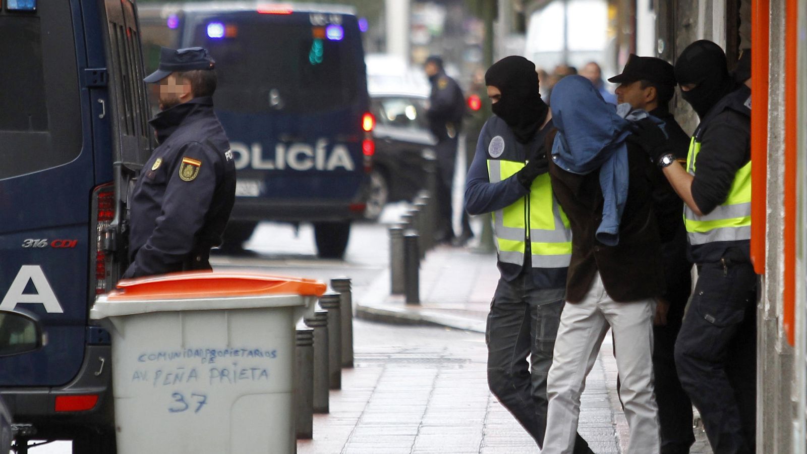 Foto: Dos efectivos de la Policía acompañan a la persona detenida hoy en el madrileño barrio de Vallecas. (EFE)