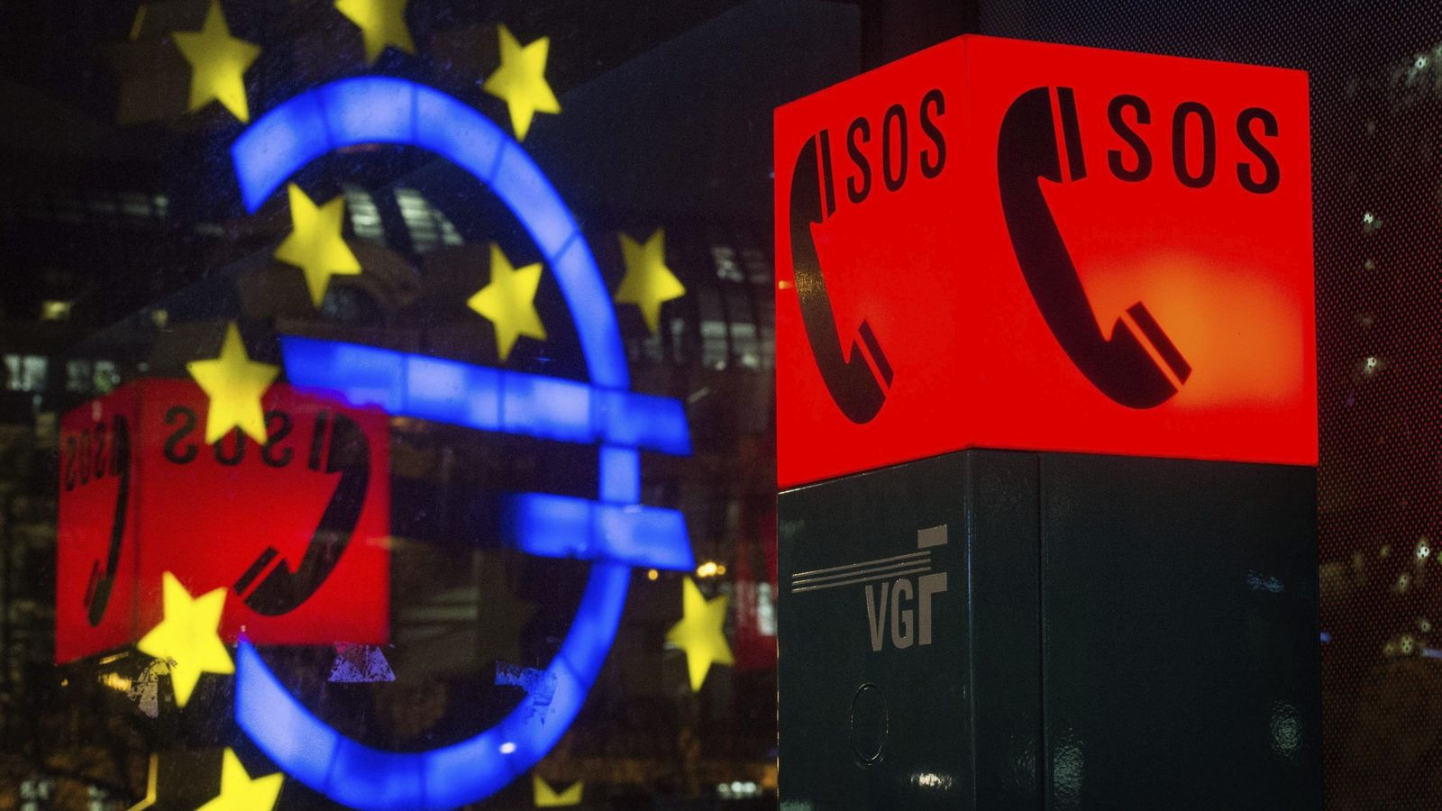 Foto: El símbolo del euro reflejado en una ventana junto al letrero luminoso de un teléfono de emergencia. (EFE)
