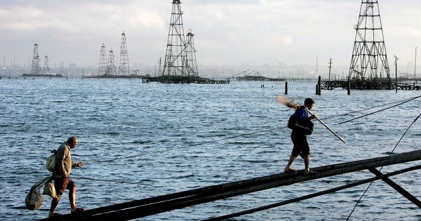 Foto: Dos trabajadores caminan frente a los pozos petrolíferos frente a las costas de Bakú, en el mar Caspio. (EFE)