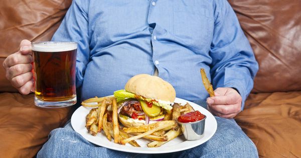 Foto: Un señor se come una hamburguesa en su sofá. (iStock)