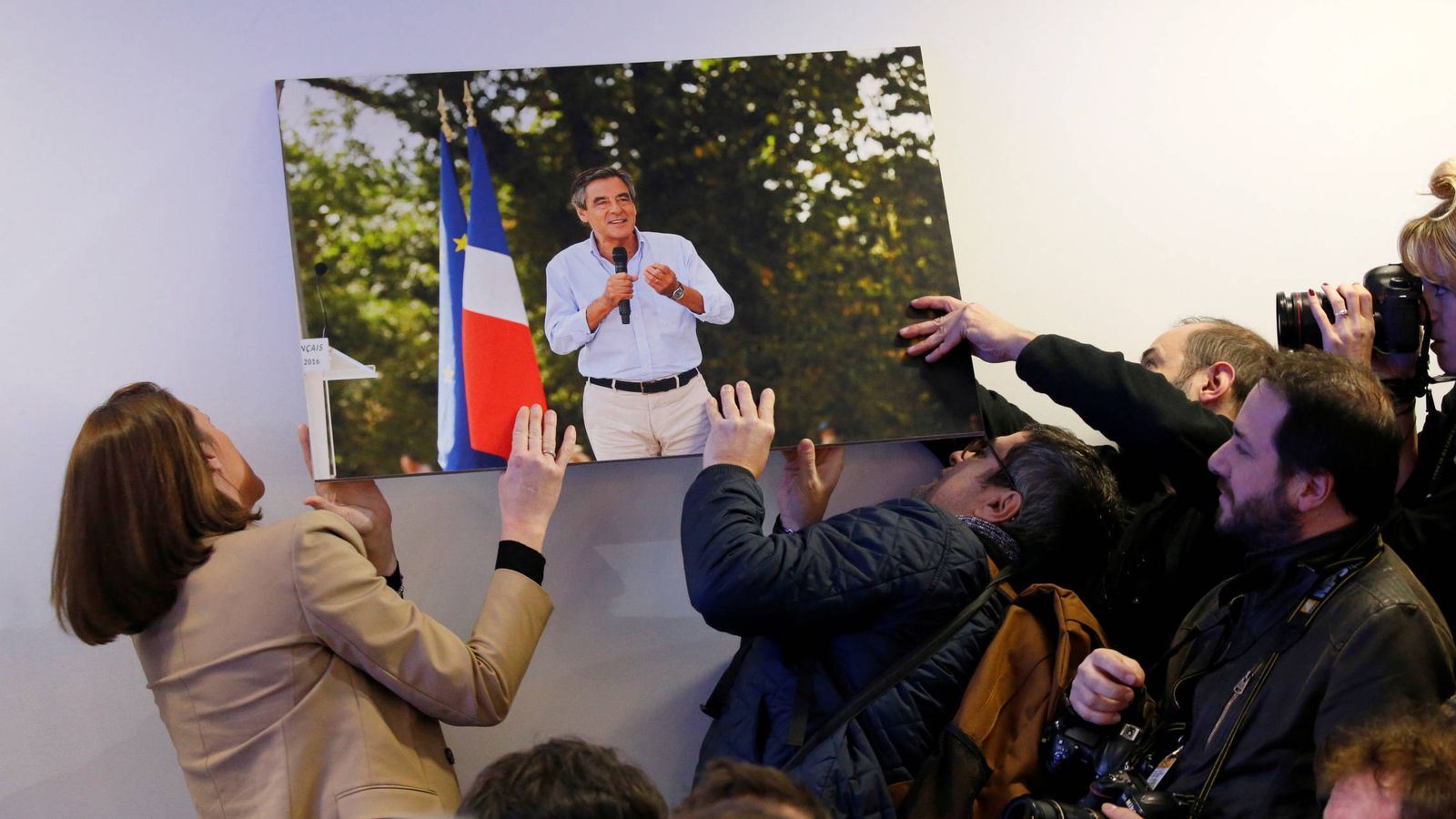 Foto: Periodistas intentan colgar una fotografía de François Fillon que se había caído antes de su rueda de prensa en París. (Reuters)