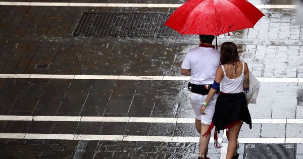 Foto: Dos personas se protegen de la lluvia en una de las céntricas calles de Pamplona, esta tarde durante la fiesta de San Fermín. (EFE)