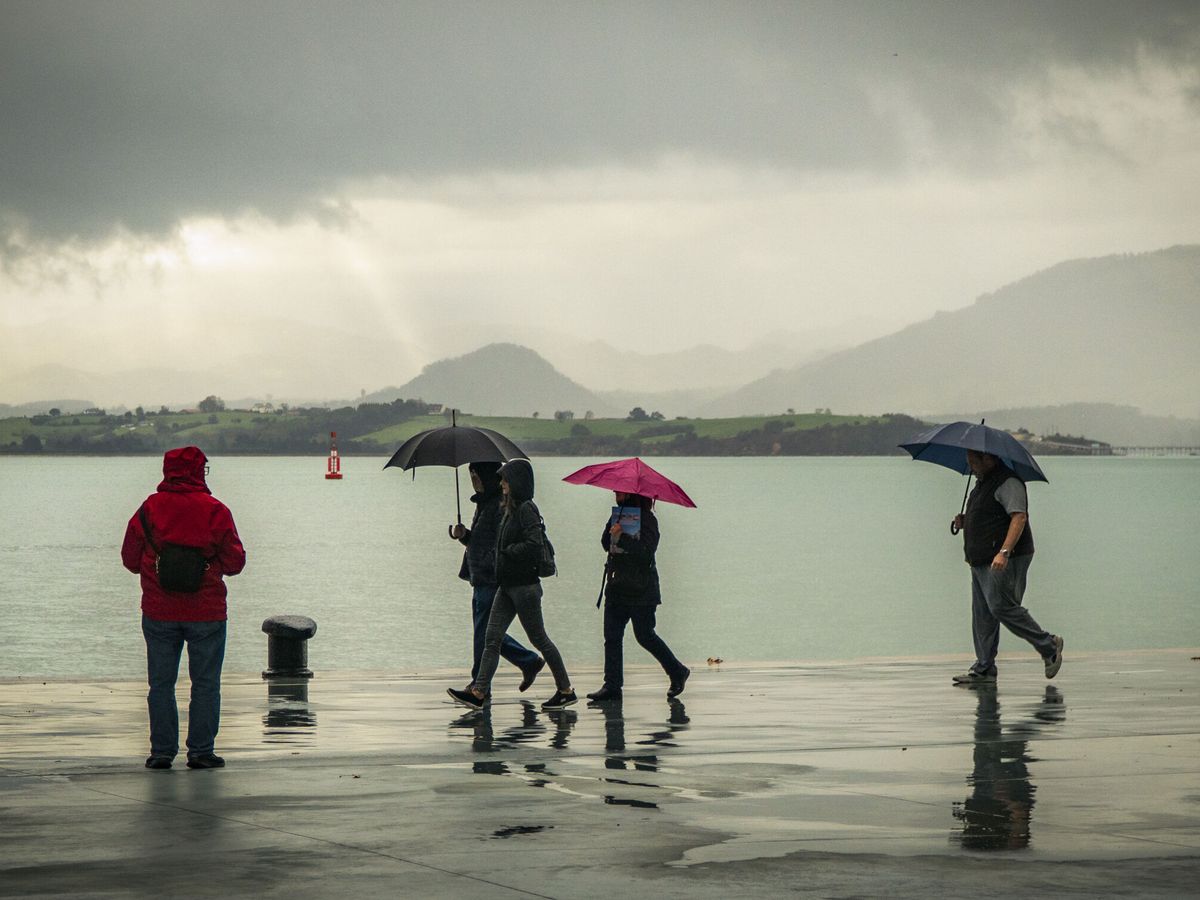 Foto: Gente pasea bajo la lluvia junto a la bahía de Santander. (EFE/Román G. Aguilera)