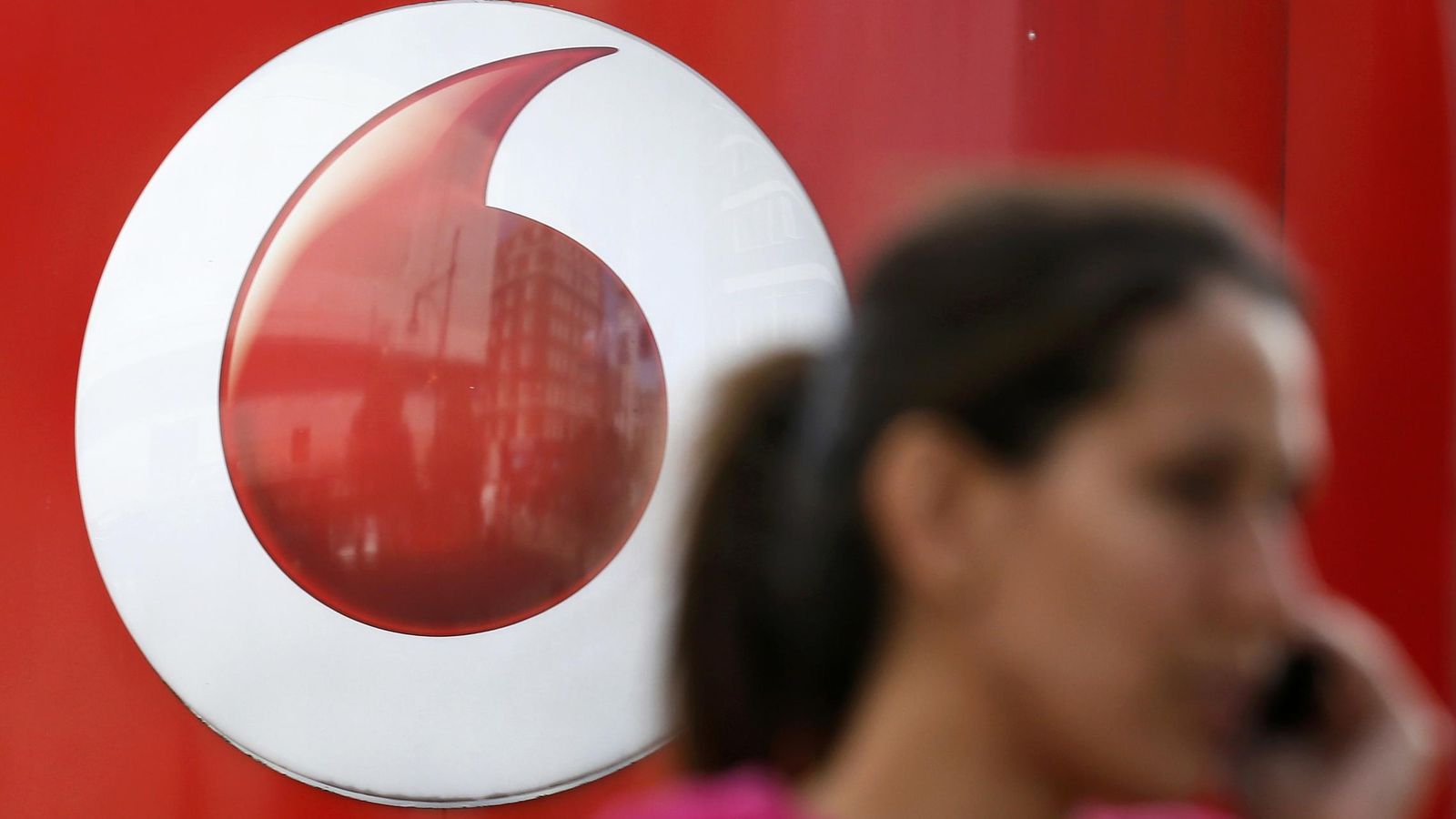 Foto: Una mujer habla por teléfono frente a un logo de Vodafone. (Reuters)
