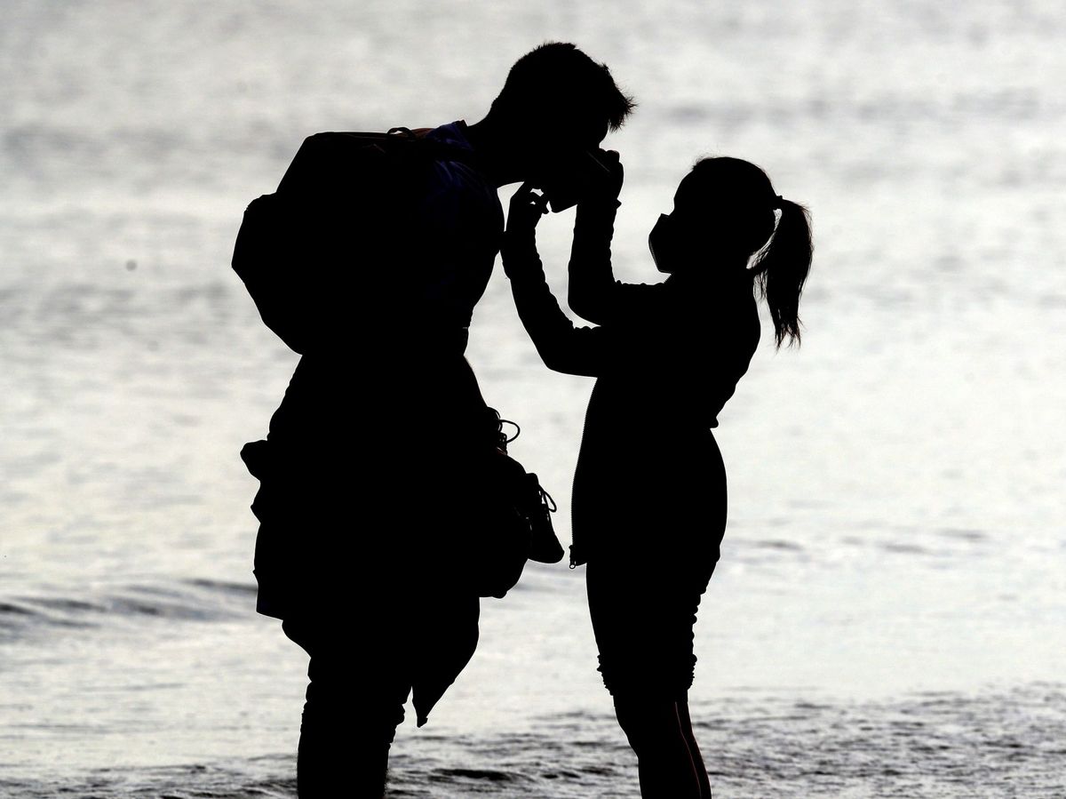 Foto: Una joven le ajusta la mascarilla a otra persona en la playa de la Malvarrosa (EFE)