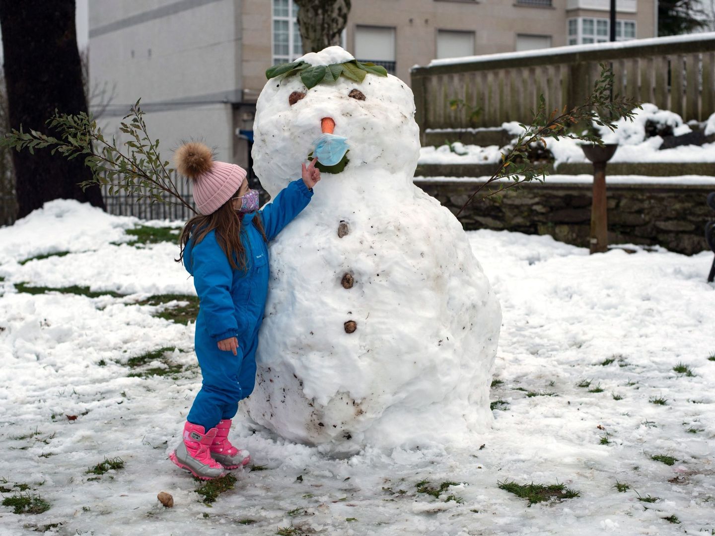 Una niña juega con un muñeco de nieve protegido con mascarilla en la localidad orensana de Castro Caldelas. (EFE)