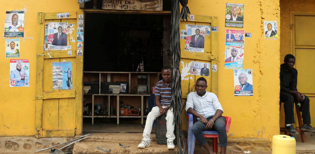 Dos ciudadanos de RDC posan junto a una pared repleta de pósters electorales de los candidatos a presidir el país. (Reuters)