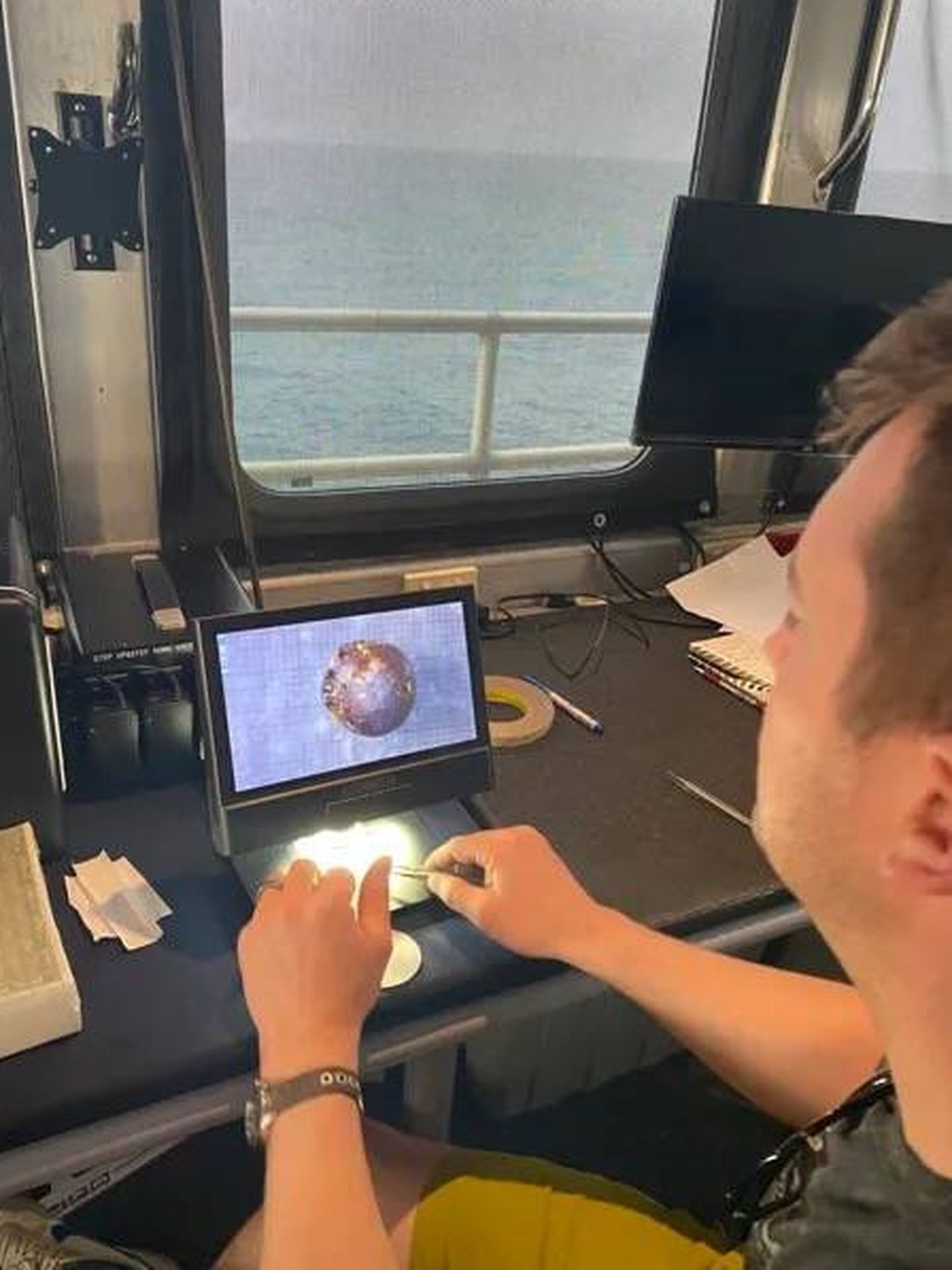 Ryan Weed utiliza un microscopio para obtener imágenes de una de las esférulas encontradas en la pasada 8 a lo largo de la trayectoria de IM1. (Avi Loeb)