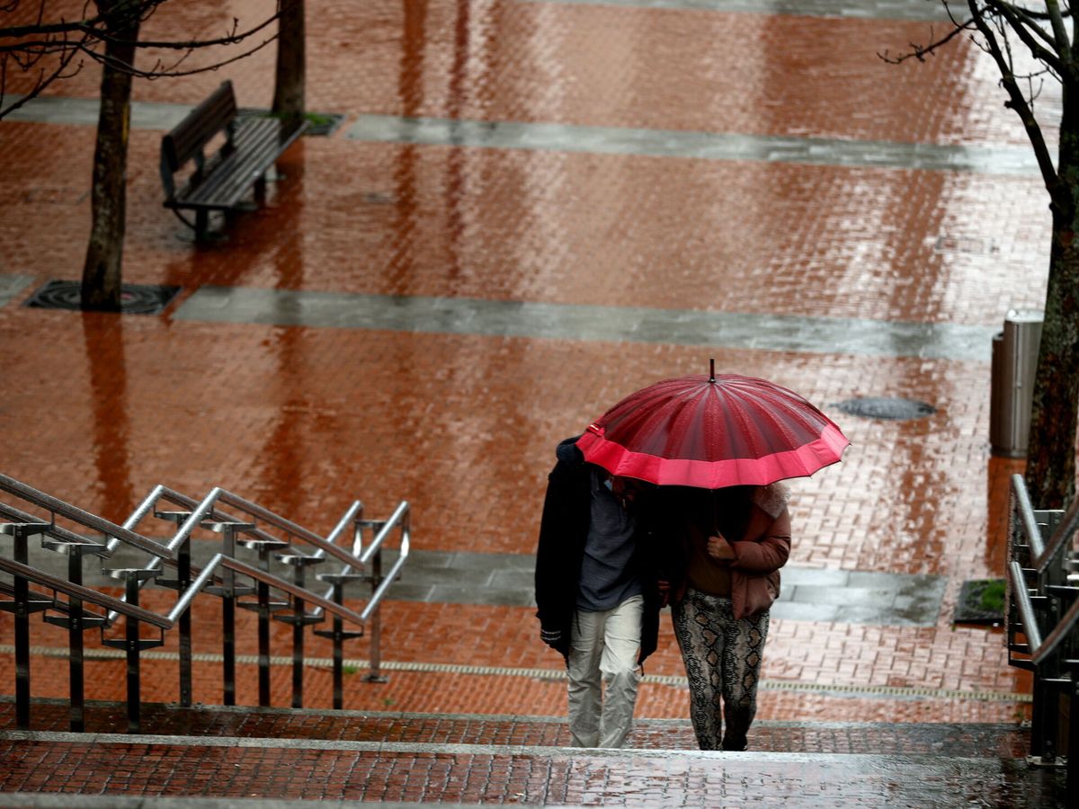 Foto: Dos personas se protegen del agua con un paraguas. (EFE/Luis Tejido)