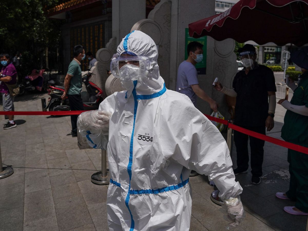 Foto: Un médico con un traje de protección es visto en las inmediaciones del hospital de Youan donde la gente hace cola para hacerse el test de coronavirus en Pekín (EFE)