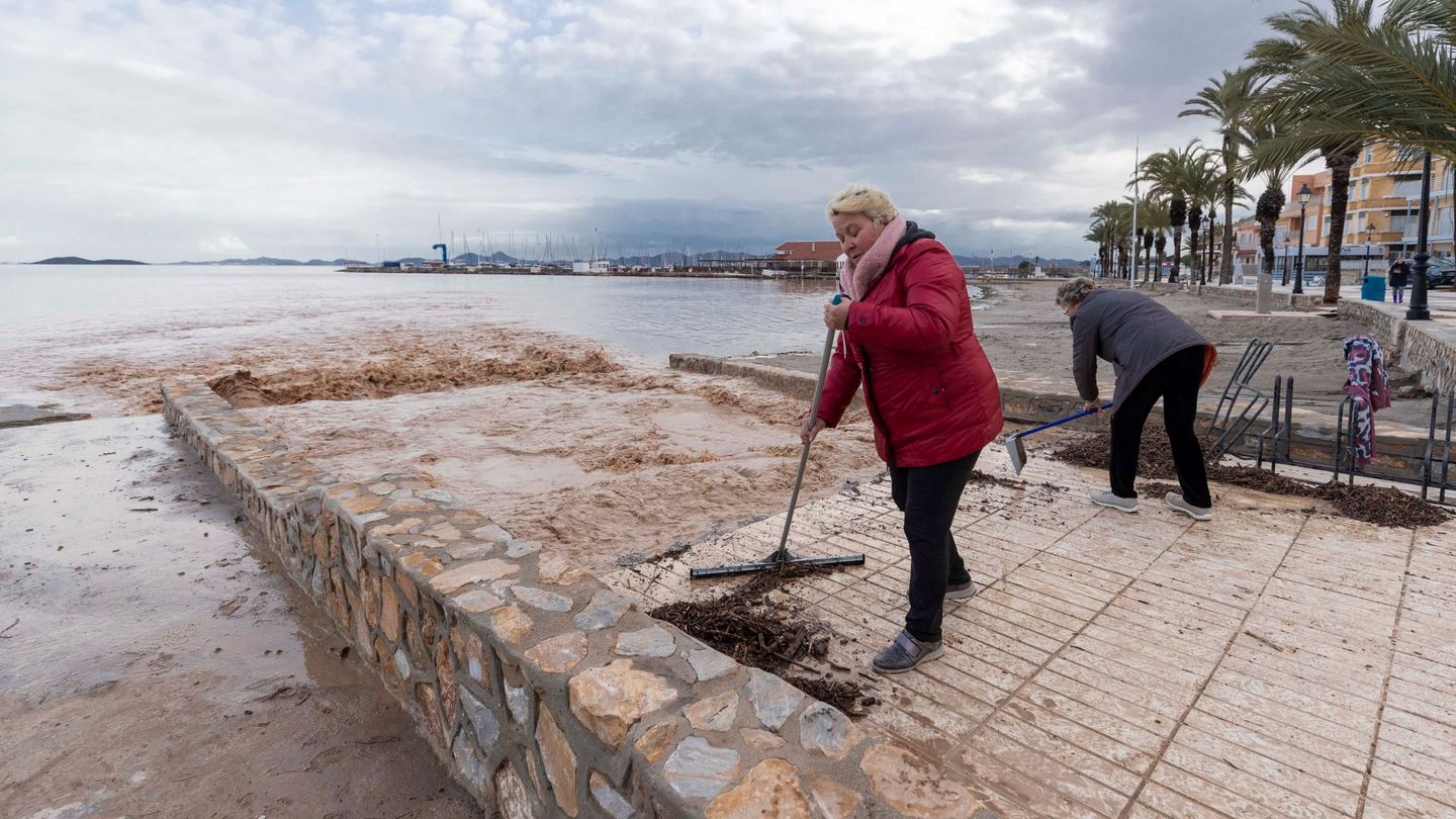 Dos vecinas de Los Alcázares retiran restos de arbustos de las aguas de lluvia que están entrando en el Mar Menor. (Marcial Guillén / EFE)