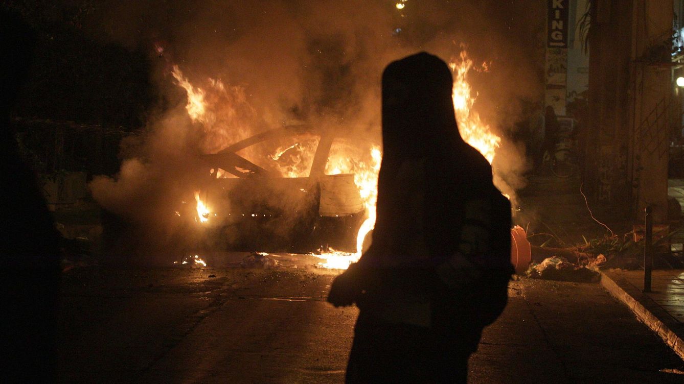 Foto: Un joven anarquista observa un coche en llamas durante enfrentamientos con la policía, en diciembre de 2014. (Reuters)