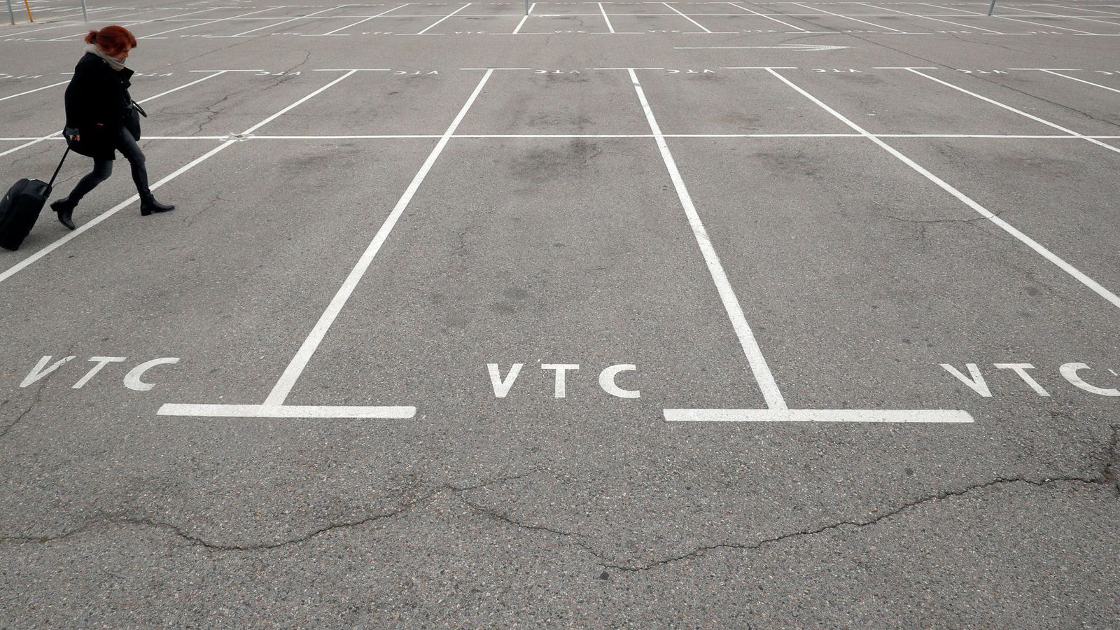 Foto: Una mujer camina por un aparcamiento vacío reservado a vehículos VTC en el aeropuerto de Barcelona. (Reuters)