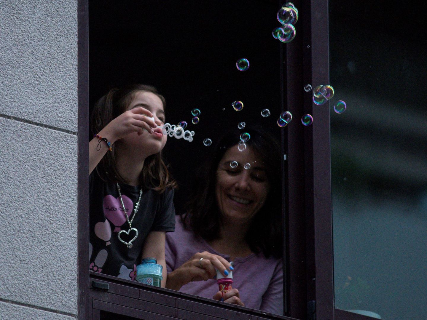 Una niña sopla pompas de jabón desde una ventana de su vivienda, ayer en Ourense. (EFE)