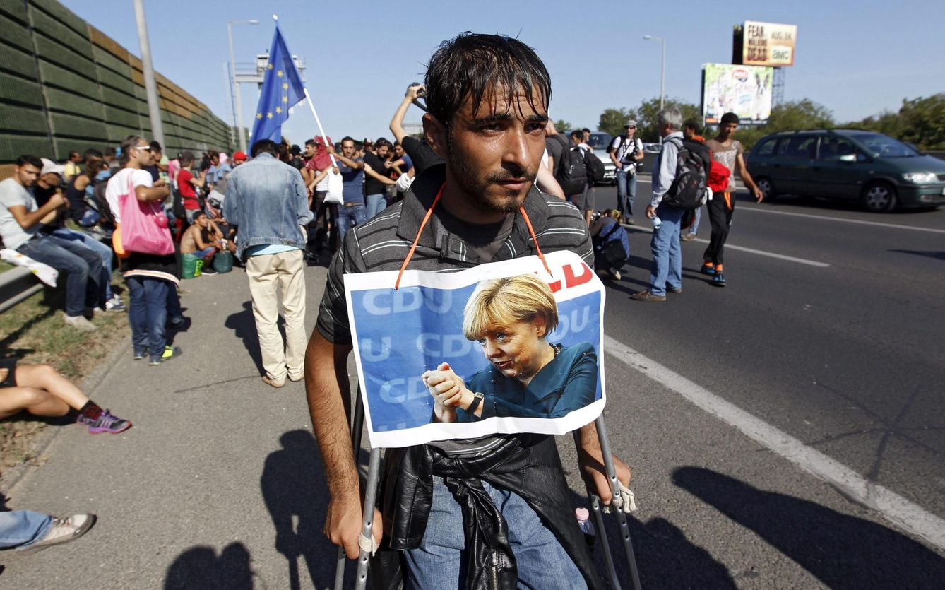 Un refugiado con un cartel colgado del cuello con la imagen de Merkel, abandona la ciudad de Budapest. (EFE)