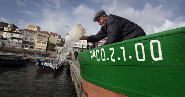 Foto: Un hombre achica agua de su barca en el puerto de Fisterra, La Coruña. (EFE)