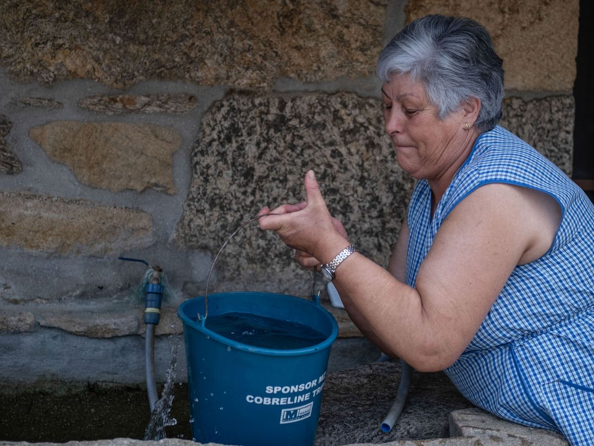 Foto: Una vecina del pueblo de San Mamede (Porqueira), recoge agua acumulada en un lavadero. (EFE/Brais Lorenzo)