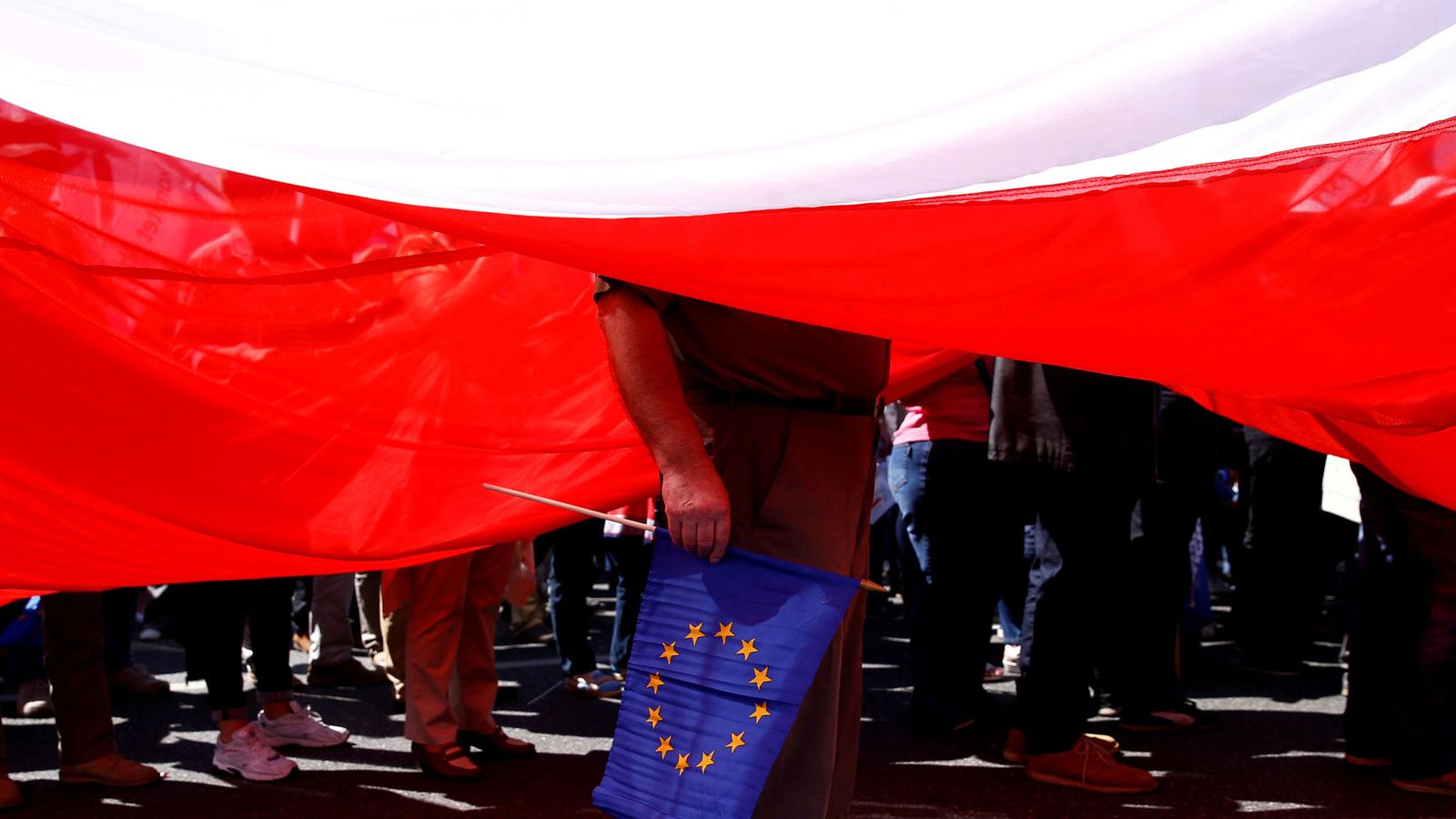 Foto: Un hombre sujeta una bandera de la Unión Europea debajo de una gigantesca bandera polaca. (Reuters)