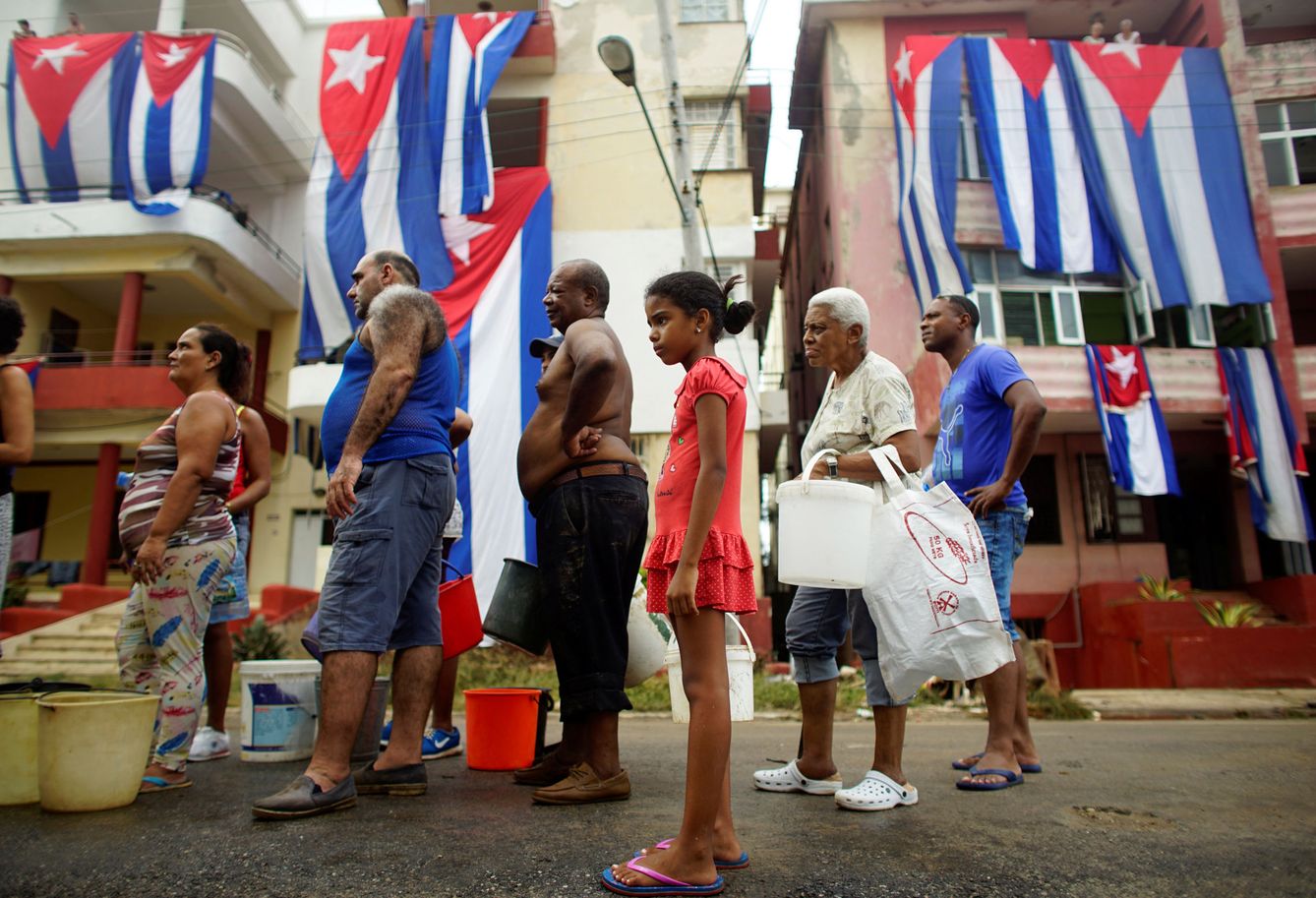 Varias personas hacen cola para recibir agua potable delante de unas banderas cubanas puestas a secar tras el paso del Irma, en La Habana, el 11 de septiembre de 2017. (Reuters)