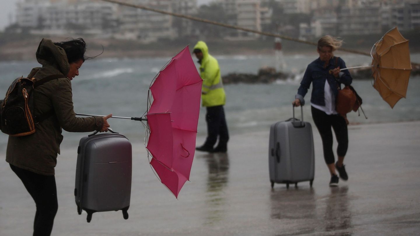 Transeúntes luchan contra el viento con sus paraguas mientras caminan junto al puerto de Rafina cerca de Atenas (Grecia). Foto: EFE