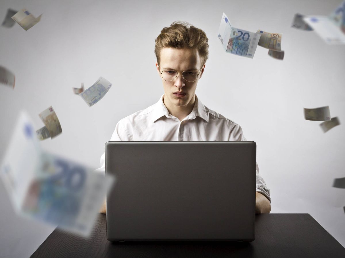 Foto: Un joven trabaja desde su portátil mientras vuelan billetes. (iStock)