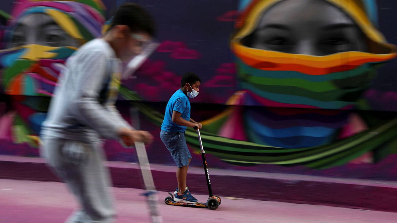 Foto: Dos niños pasan con sus patinetes frente a un mural en Chile. (Reuters)