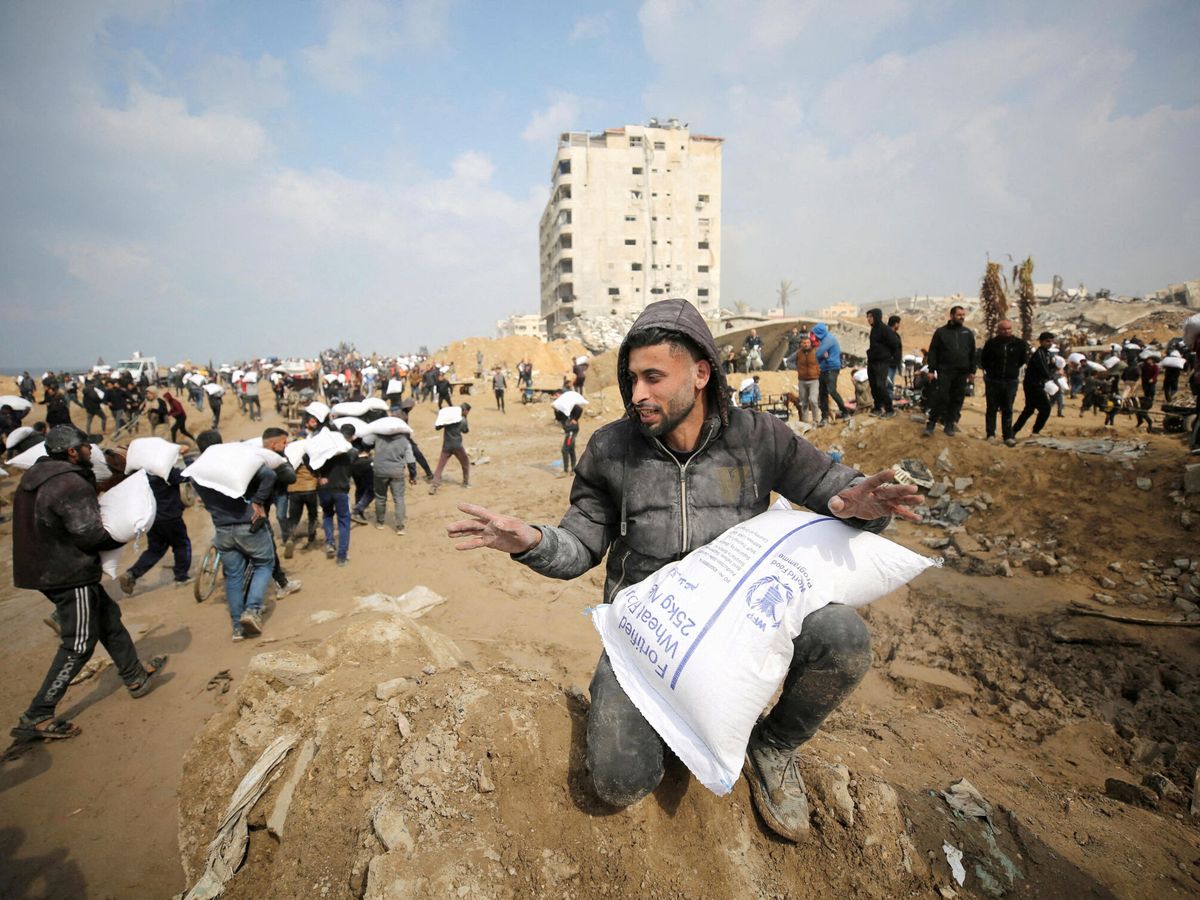 Foto: Palestinos con sacos de harina entregada por la escasa ayuda humanitaria. (Reuters/Kosay Al Nemer)
