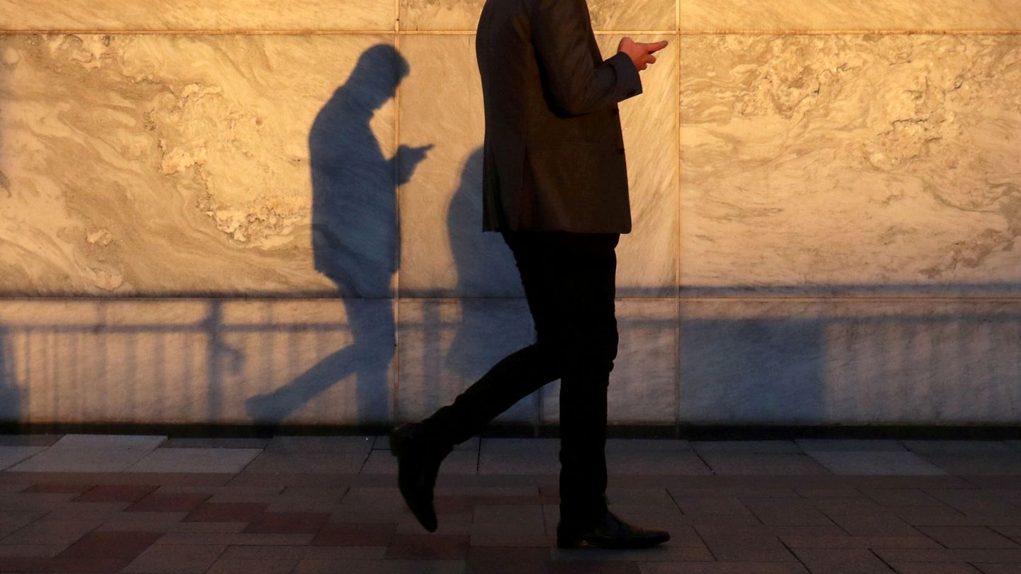 FILE PHOTO: An unidentified man using a smart phone walks through London's Canary Wharf financial district in the evening light in London, Britain, September 28, 2018.   REUTERS Russell Boyce File Photo