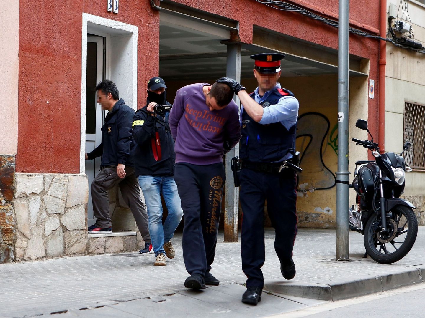 Un Mosso d'Esquadra custodia a uno de los dos detenidos en Cornellà de Llobregat. (EFE)