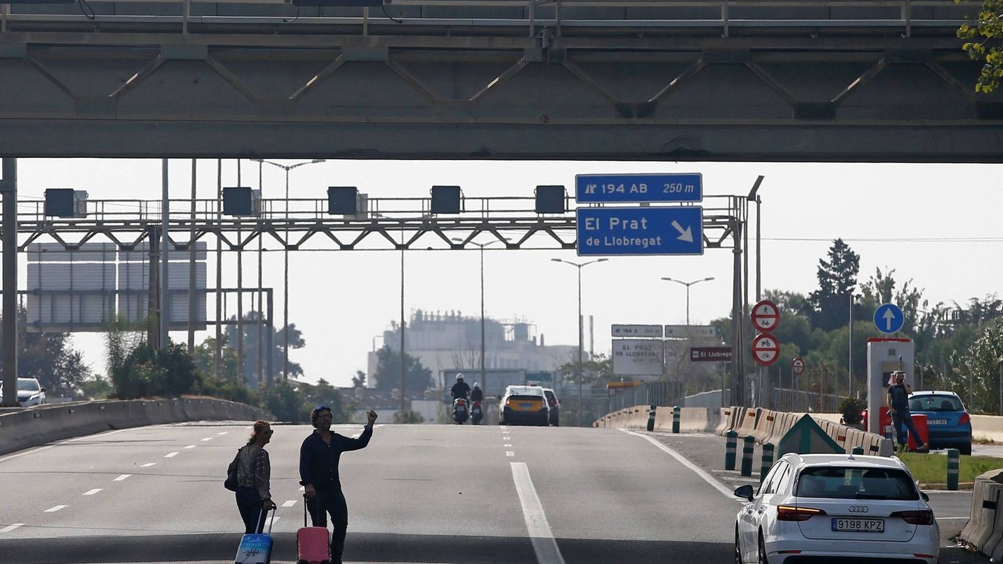 Dos viajeros tratan de llegar al aeropuerto de El Prat, bloqueado por los manifestantes. (EFE)