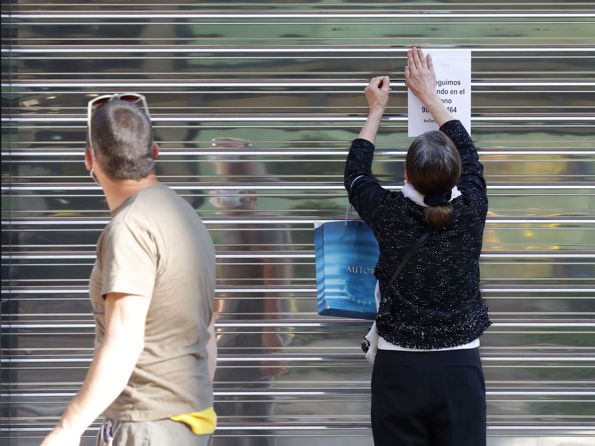 Foto: Una mujer coloca un aviso en la persiana cerrada de un negocio del centro de Oviedo. (EFE)