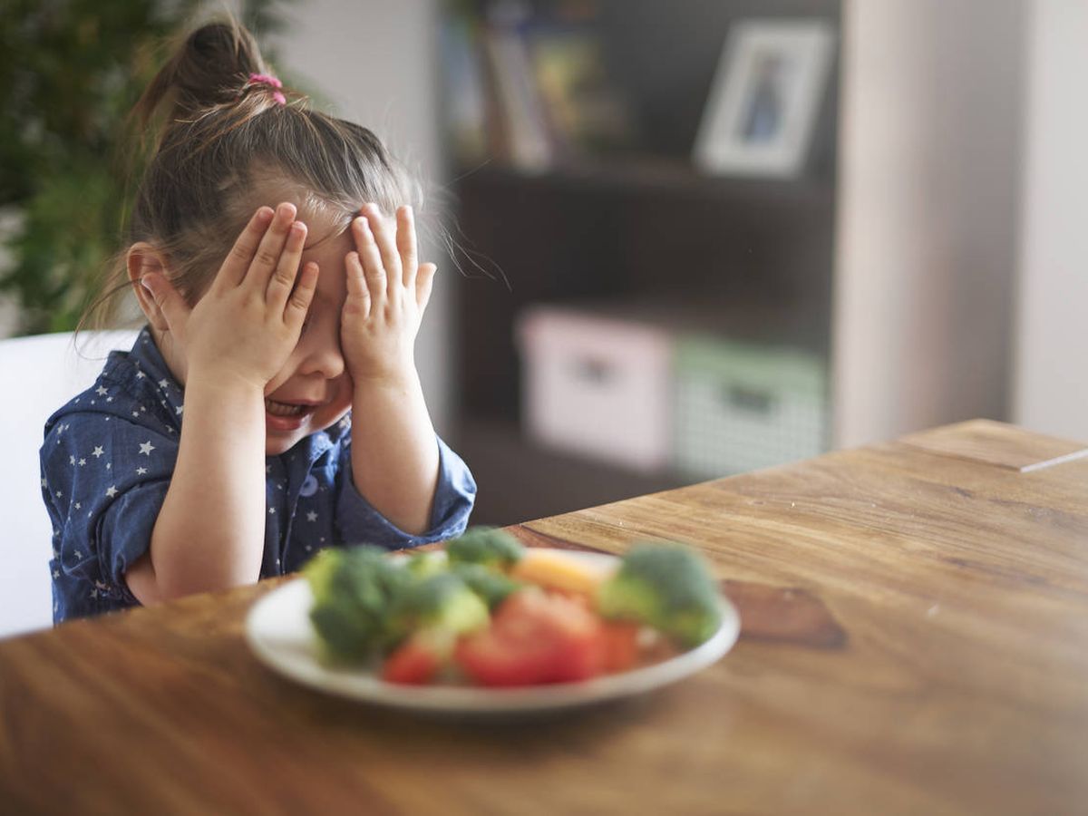 Foto: Una niña se echa las manos a la cabeza frente a un plato de verduras. (iStock)