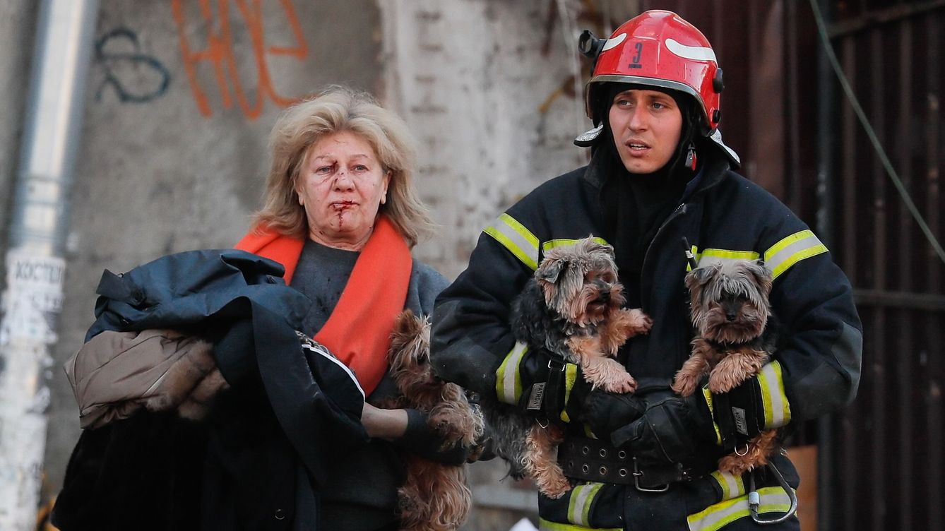 Foto: Una mujer herida en el bombardeo contra Kiev junto a un bombero que la ayuda a cargar sus perros. (EFE/Sergey Dolzhenko)