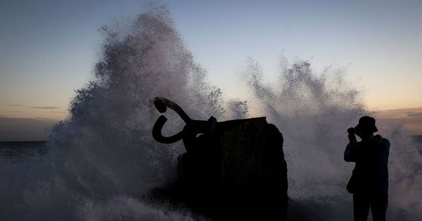 Foto: Una persona fotografía una ola al romper en el Peine del Viento. (EFE)