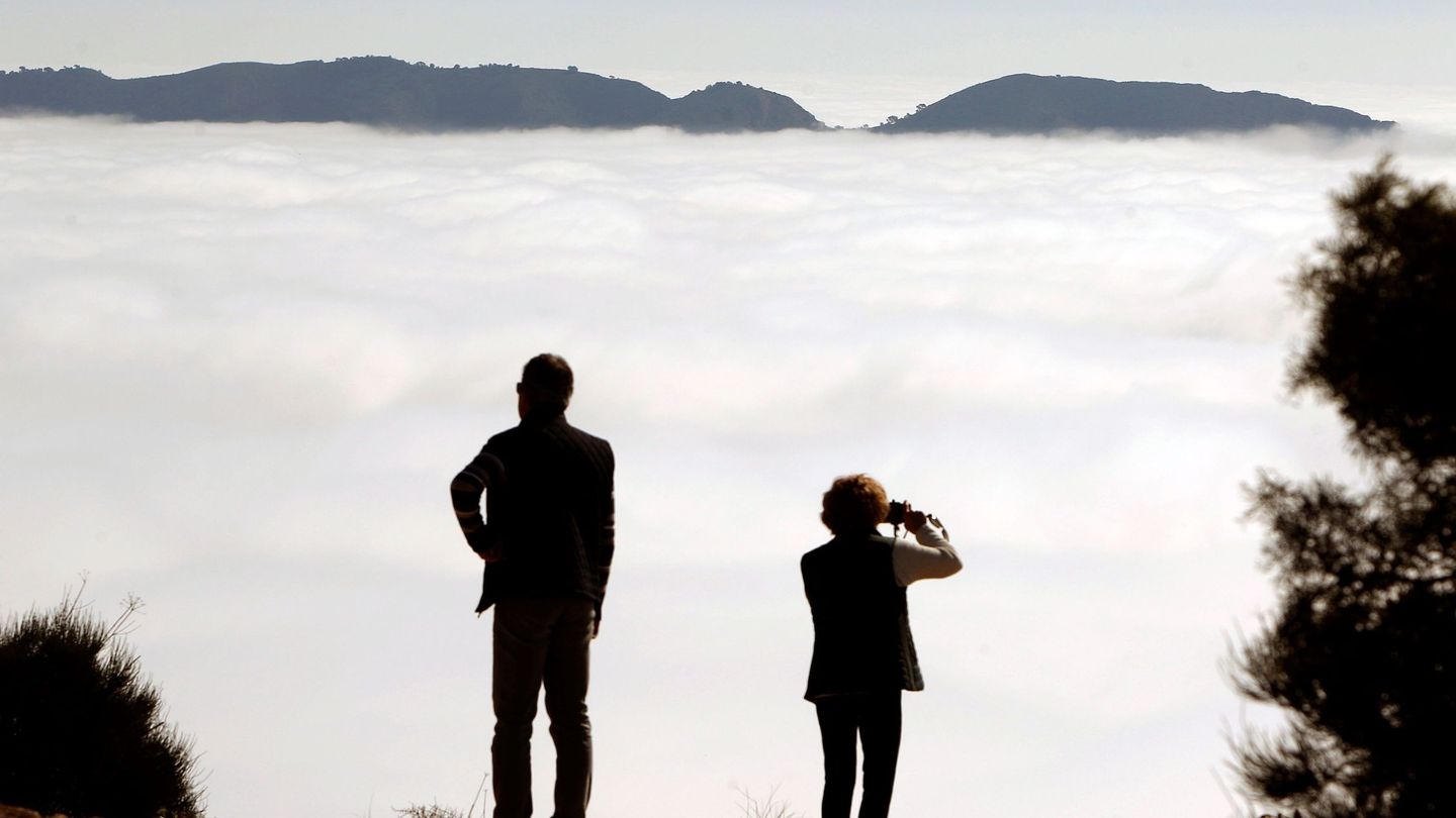 Dos personas contemplan Sierra Helada con un Benidorm completamente cubierto por la niebla. (EFE/Morell)